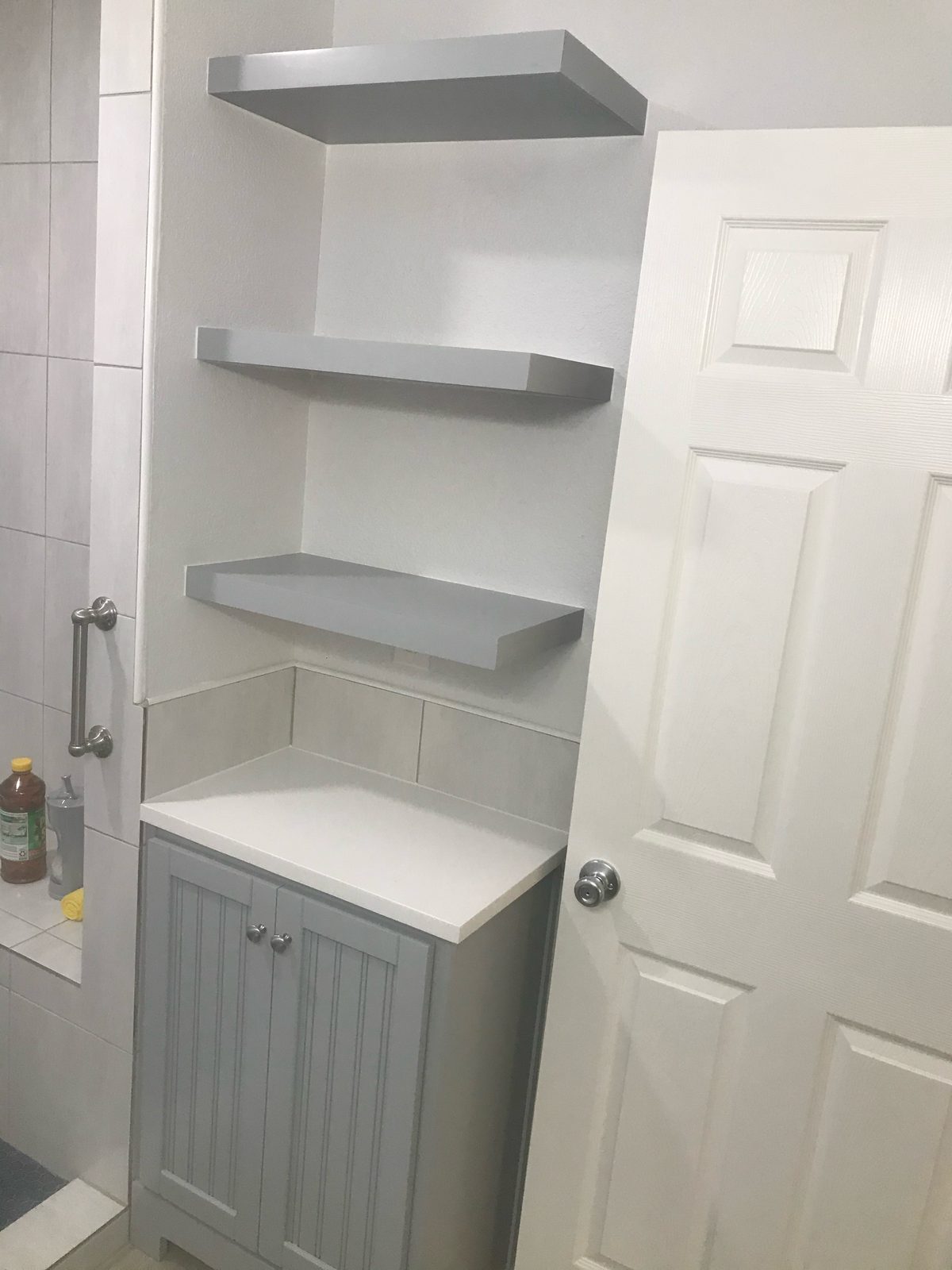 Gray beadboard bathroom cabinet with floating shelves above