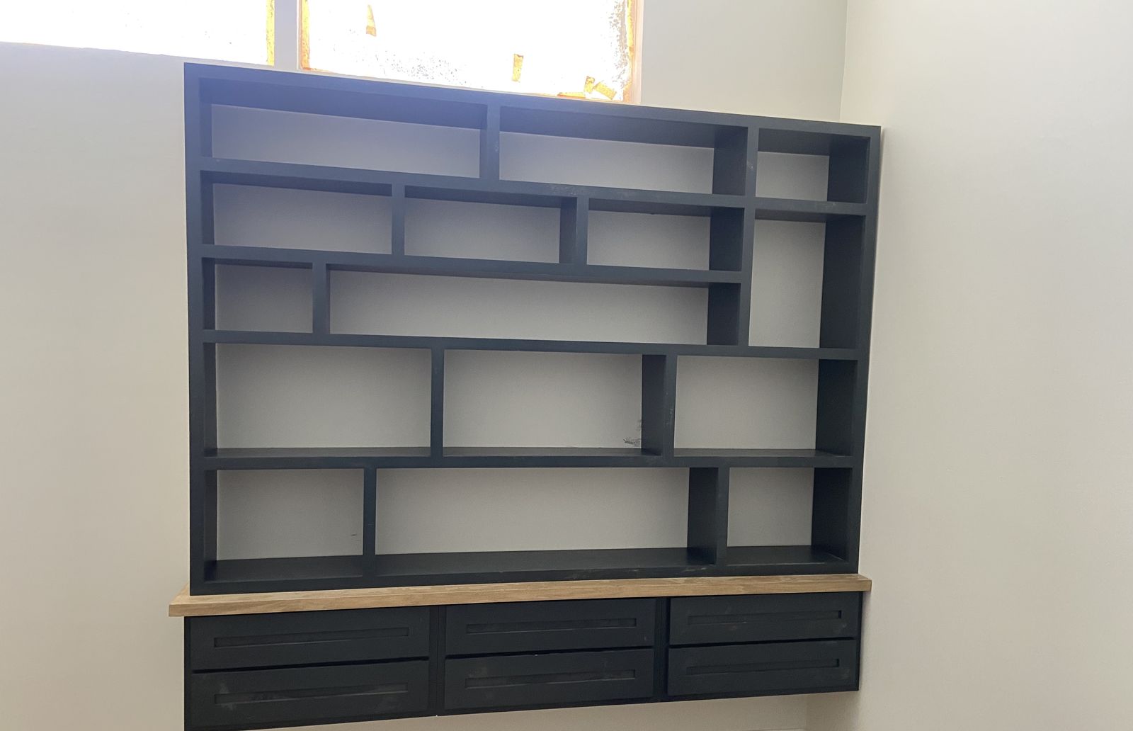 Black floating geometric bookshelf with drawers and a wood top