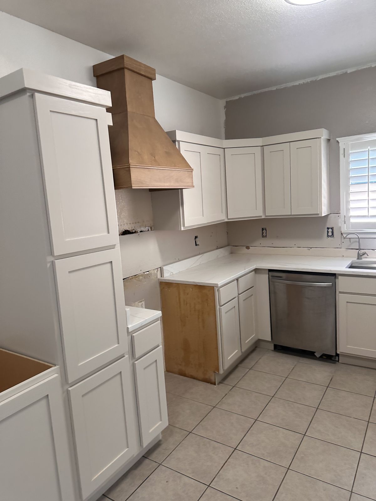 White shaker kitchen with a stained wood range hood before backsplash