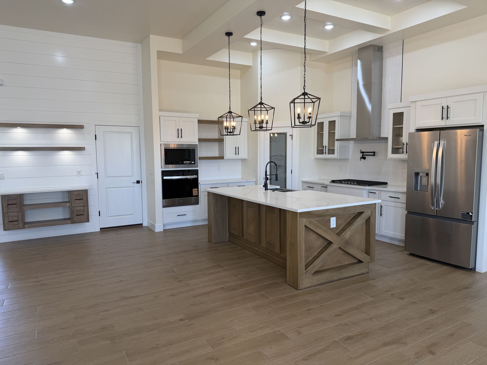 Bright white shaker kitchen with a natural wood X-panel island, open shelves and lantern pendant lights