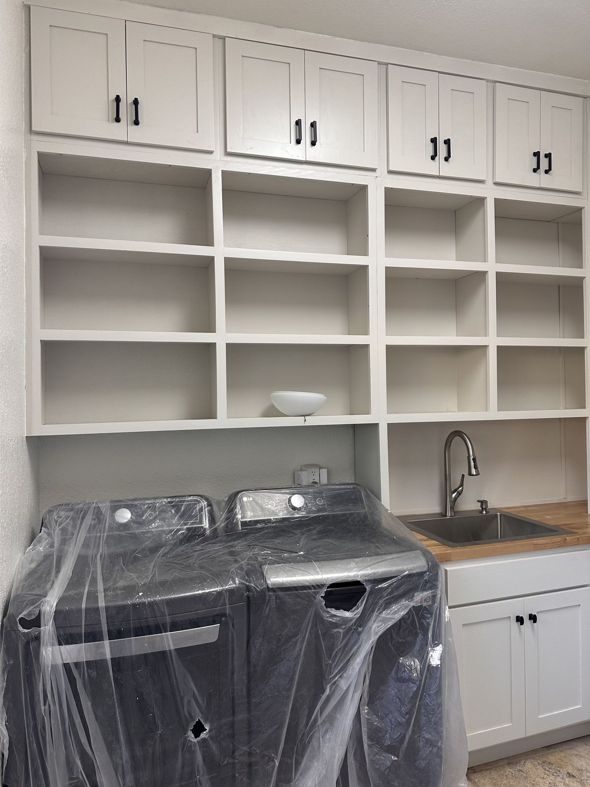 White laundry room cabinets with open cubby shelves and a utility sink